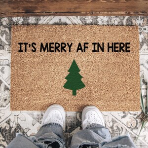 It's merry AF in here doormat with a green tree viewed from above with white shoes at the edge.