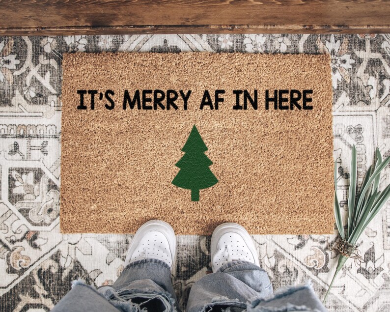 It's merry AF in here doormat with a green tree viewed from above with white shoes at the edge.