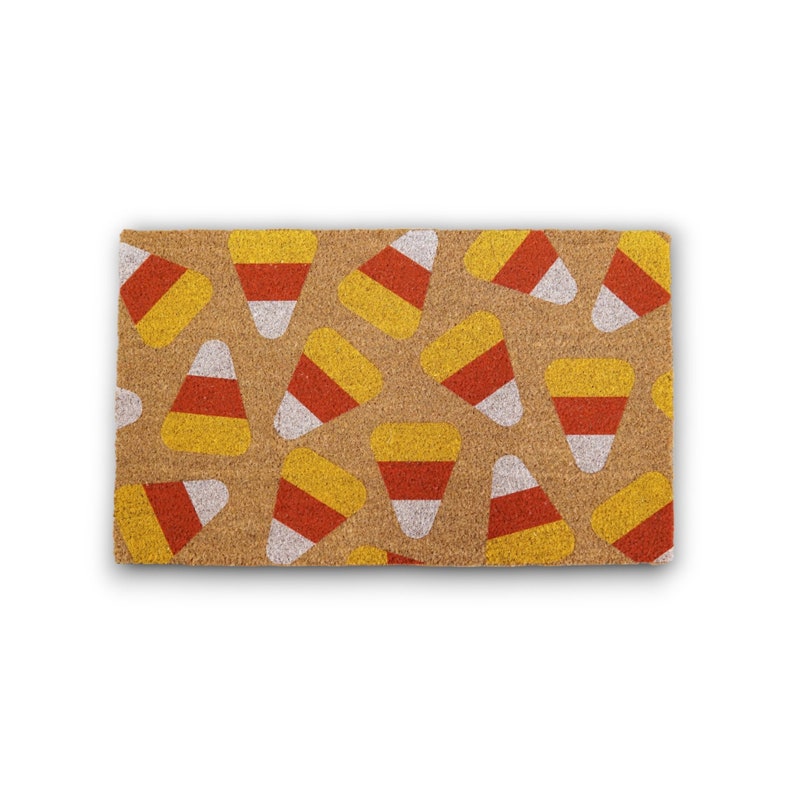 May include: A brown coir doormat with a pattern of yellow, orange and white candy corn.