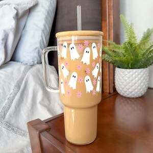 Large handled glass tumbler with white ghosts and pink flowers, filled with iced coffee on a bedside table.
