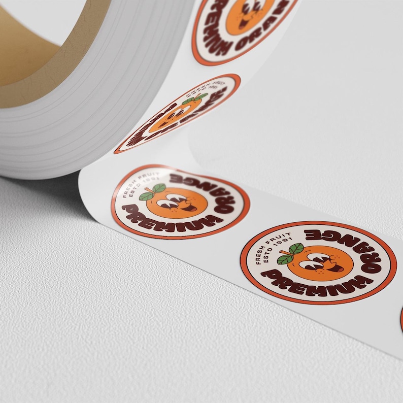 Roll of round orange-and-cream logo stickers unspooled on a white surface, showing a smiling orange fruit design.