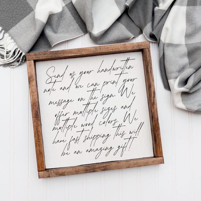 Brown framed sign with sample handwriting explaining custom handwritten message printing, beside a checked blanket.