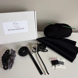 Può includere: Un kit fai-da-te per cappuccio per cavalli con una scatola bianca con l'etichetta "DIY Horse Bonnet Kit". Il kit include filato nero, tessuto, finiture decorative, filo, aghi e cordoncino. Il kit è progettato per la creazione di cappucci per cavalli.