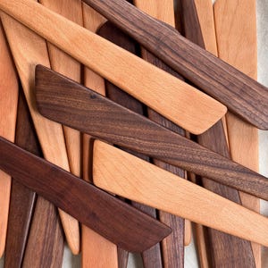 K&ouml;nnte beinhalten: Eine Auswahl an Holzspateln in verschiedenen Braunt&ouml;nen. Einige Spatel sind hellbraun, andere dunkelbraun. Die Spatel bestehen aus verschiedenen Holzarten und sind leicht &uuml;berlappend angeordnet. Das Bild zeigt eine Vielzahl von K&uuml;chenutensilien.