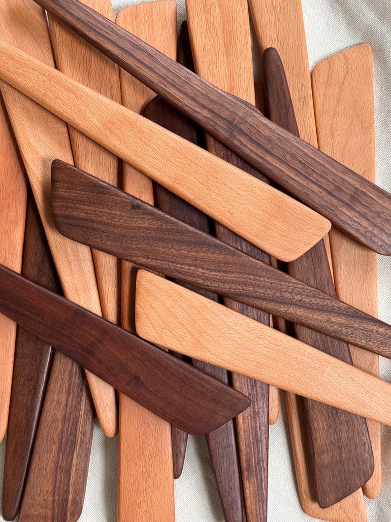 K&ouml;nnte beinhalten: Eine Auswahl an Holzspateln in verschiedenen Braunt&ouml;nen. Einige Spatel sind hellbraun, andere dunkelbraun. Die Spatel bestehen aus verschiedenen Holzarten und sind leicht &uuml;berlappend angeordnet. Das Bild zeigt eine Vielzahl von K&uuml;chenutensilien.