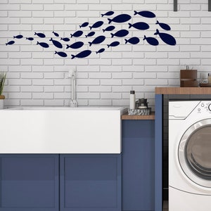 Può includere: Un lavello in porcellana bianca in stile farmhouse con un mobiletto blu sottostante. Il lavello è installato in una parete di mattoni bianchi con un banco di adesivi di pesci blu sul muro sopra il lavello.
