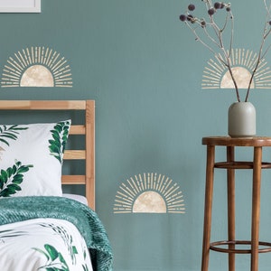 May include: A bedroom scene with a teal wall adorned with beige sunburst wall decals. A wooden bed frame supports a bed with a white floral patterned duvet and green throw blanket. A framed botanical print hangs on the wall.