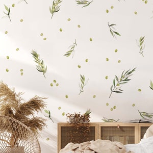 May include: A white bedroom with a bed with white bedding and a tan throw blanket. The wall behind the bed has a white background with a pattern of green olive branches and green dots.