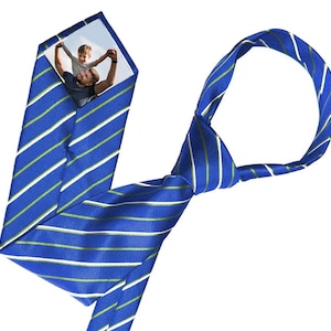 Può includere: Una cravatta a righe blu e bianche con una riga verde. Una foto di un padre e un figlio è visibile attraverso la cravatta.