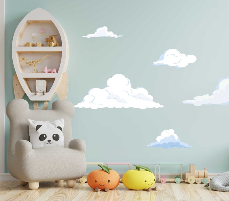 K&ouml;nnte beinhalten: Eine hellblaue Wand mit wei&szlig;en Wolken und einem wei&szlig;en Raketenregal mit Spielzeug darauf. Vor dem Regal steht ein grauer Sessel mit einem Pandakissen. Auf dem Boden liegen zwei orangefarbene und gelbe Spielzeuge in Form von Fr&uuml;chten.