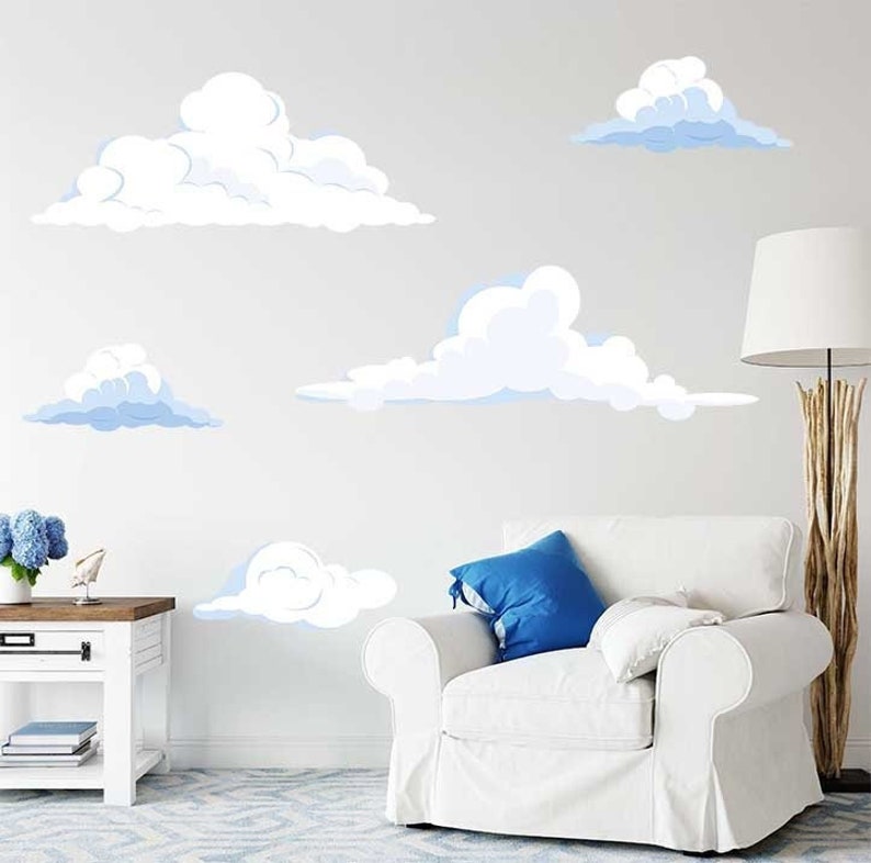 K&ouml;nnte beinhalten: Ein wei&szlig;er Sessel mit einem blauen Kissen vor einer wei&szlig;en Wand mit blauen und wei&szlig;en Wolken-Wandaufklebern.