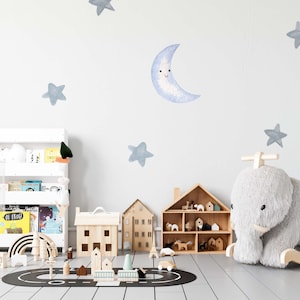 Peut inclure: Une étagère blanche avec des livres et des jouets, une maison en bois, un cheval à bascule en bois en forme d'éléphant et un tapis de route noir et blanc sur un sol en bois clair. Le mur est décoré d'étoiles bleues en aquarelle et d'un croissant de lune.
