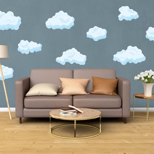 May include: A living room scene with a gray sofa, decorative pillows, and a round coffee table. The wall is adorned with light blue cloud decals. A floor lamp with a beige shade and a small side table with a vase of white flowers complete the decor.