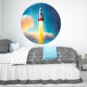 May include: A white and red rocket ship blasts off into a blue sky with white clouds. The rocket ship is surrounded by a circle of stars.