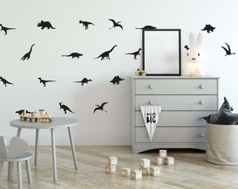 May include: A white wall with black dinosaur silhouettes, a white dresser with a white banner that says "Dream Big", a white bunny lamp, a grey toy chair, a wooden toy train, and wooden alphabet blocks.