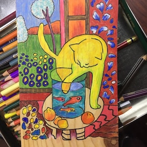 May include: A colorful, hand-drawn illustration on wood depicts a yellow cat reaching into a fishbowl with orange fish. The scene includes a window, trees, and fruit. The artwork is surrounded by colored pencils.