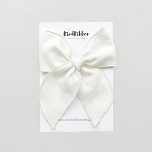 Puede incluir: Un lazo de tela blanco con un borde cosido. El lazo está sobre una tarjeta blanca con el texto "Kindribbon Handmade Hair Accessories www.kindribbon.etsy.c"