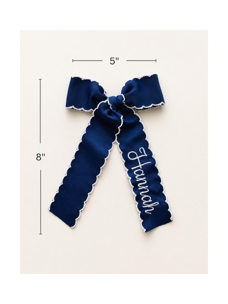 Peut inclure: Un n&oelig;ud pour cheveux bleu marine avec des bords festonn&eacute;s blancs et le pr&eacute;nom Hannah brod&eacute; en &eacute;criture blanche sur un pan. Le n&oelig;ud mesure 5 pouces de largeur et 8 pouces de longueur, comme indiqu&eacute; par les lignes et le texte de mesure.
