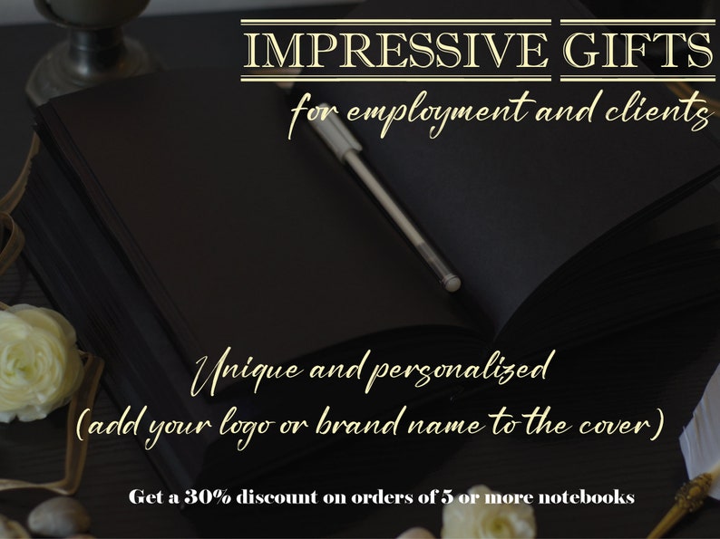 May include: A black leather bound notebook with a silver pen lying on top. The notebook is on a dark wooden surface with white flowers and a gold pen. The text on the image reads "IMPRESSIVE GIFTS for employment and clients Unique and personalized (add your logo or brand name to the cover) Get a 30% discount on orders of 5 or more notebooks".