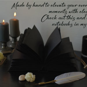May include: A black leather bound journal with a feather pen on a dark wooden surface. The journal is open and the pages are blank. There are candles and other decorative items on the surface. The text "Made by hand to elevate your everyday moments with elegance. Check out this and other notebooks in my store." is visible in the image.