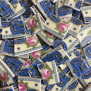 May include: A pile of blue and white ceramic tiles with a floral pattern. The tiles are broken into various shapes and sizes. The floral pattern features pink roses and green leaves.