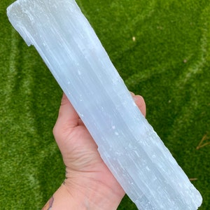 May include: A large, white selenite crystal slab with a smooth, striated surface. The crystal is held in a hand, showcasing its size and texture.