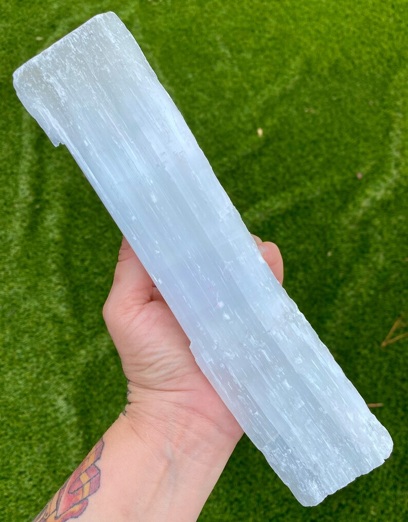 May include: A large, white selenite crystal slab with a smooth, striated surface. The crystal is held in a hand, showcasing its size and texture.