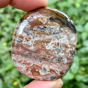 May include: A polished, oval-shaped stone with a swirling pattern of brown, white, and black. The stone has a smooth, polished surface.