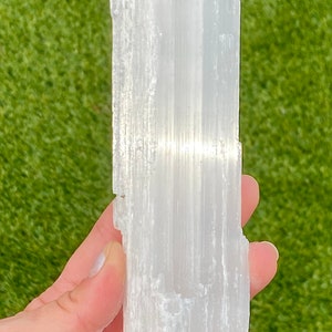 May include: A white selenite crystal wand with a smooth, striated surface. The wand is approximately 6 inches long and 2 inches wide.