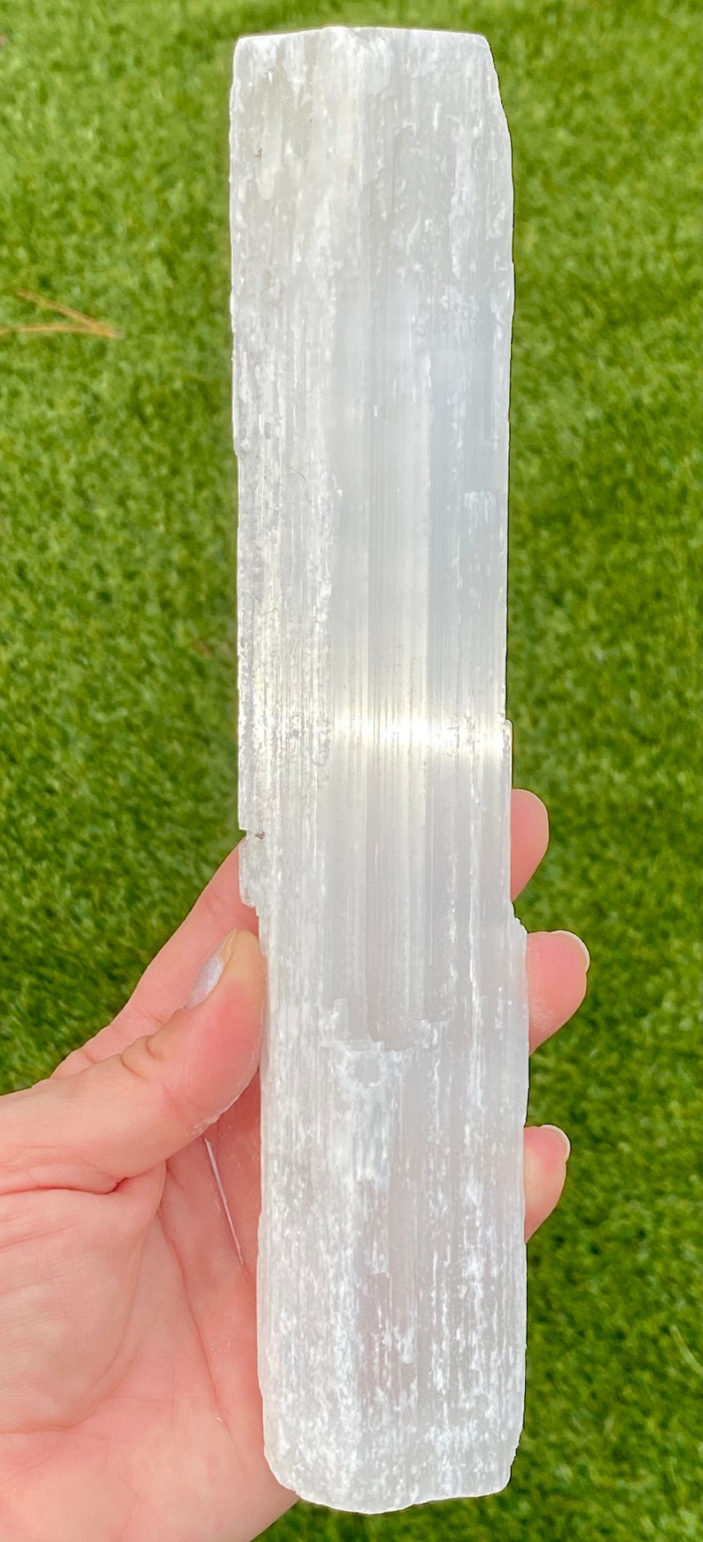 May include: A white selenite crystal wand with a smooth, striated surface. The wand is approximately 6 inches long and 2 inches wide.