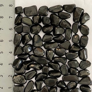 May include: A collection of polished, medium-sized, black hematite stones. The stones are smooth and reflective, with a dark, metallic sheen. The word "Medium" is printed in large, black letters at the top of the image. A ruler is in the image.