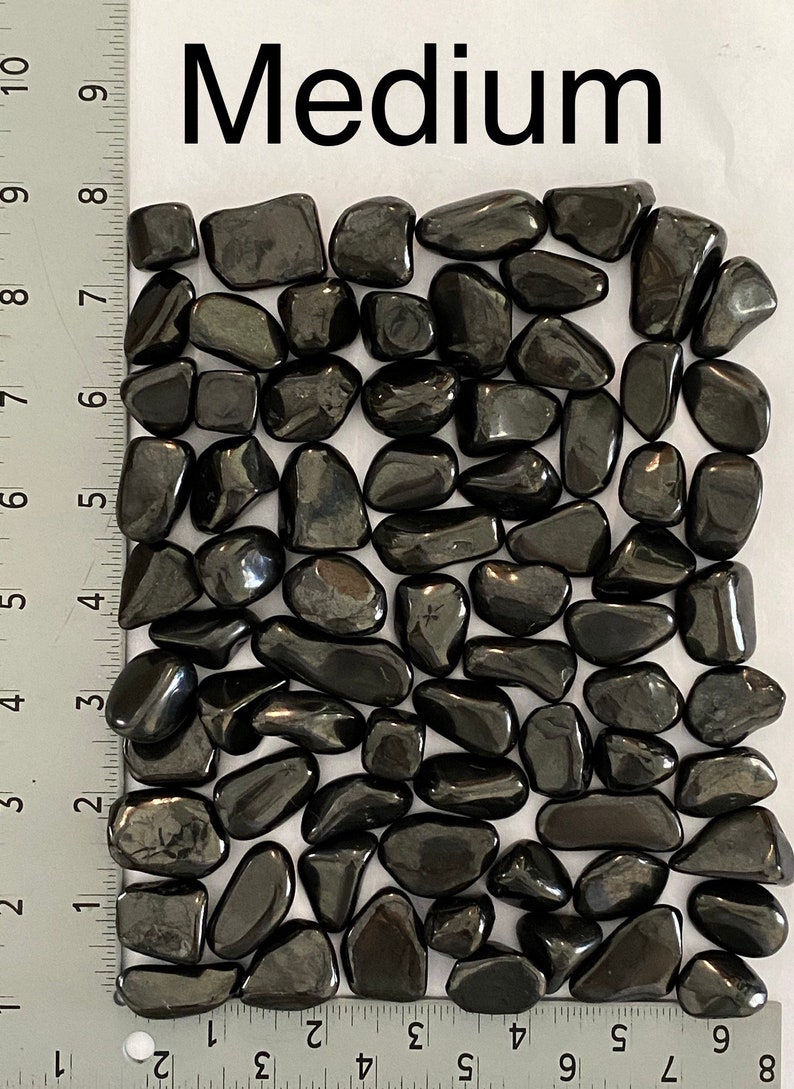 May include: A collection of polished, medium-sized, black hematite stones. The stones are smooth and reflective, with a dark, metallic sheen. The word "Medium" is printed in large, black letters at the top of the image. A ruler is in the image.