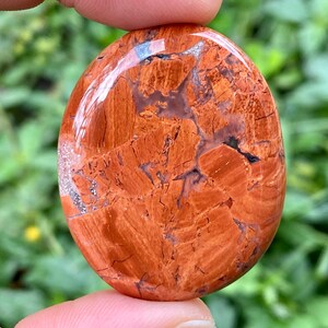 May include: A smooth, polished red jasper stone with white and black veins. The stone is oval shaped and has a glossy finish.