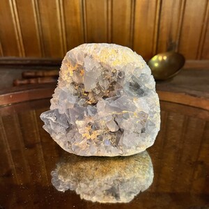 May include: A light blue crystal cluster with a natural, rough texture. The crystal has a white, cloudy appearance and is accented with gold flecks.