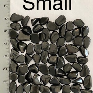 May include: A collection of small, polished, black stones. The stones are smooth and rounded, with a glossy finish. The word "Small" is printed in large black letters above the stones. The stones are measured using inches.