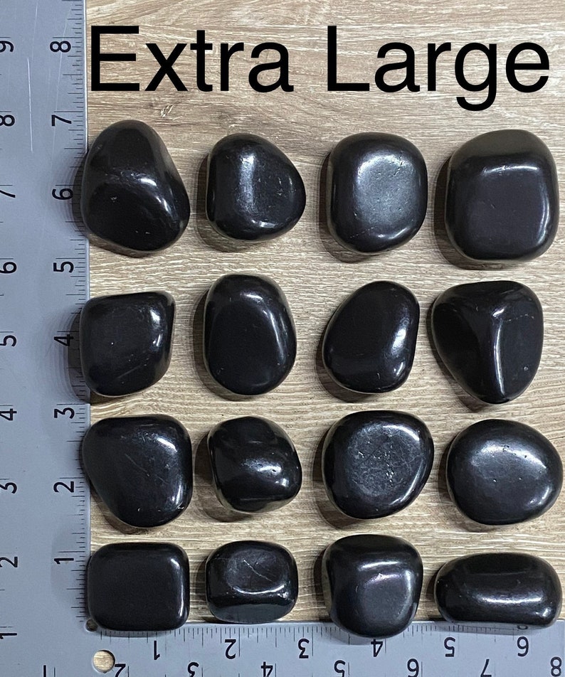 May include: Extra Large black polished stones. The stones are smooth and vary in shape, with rounded and rectangular forms. The image includes a ruler for size reference. The text "Extra Large" is at the top.