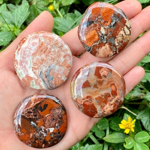 May include: Four smooth, round, polished stones with a red, brown, and white marbled pattern. The stones are about the size of a silver dollar.