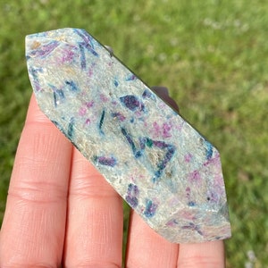 May include: A polished, double-terminated crystal point with a white, gray, blue, and pink color pattern. The crystal is a natural, raw, and rough gemstone.