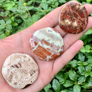 May include: Three smooth, polished, round stones with a red, white, and brown marbled pattern. The stones are in the palm of a hand.
