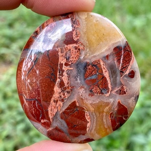 May include: A polished red, white, and brown jasper stone with a unique, swirling pattern. The stone is smooth and has a natural, organic look.