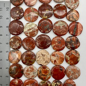 May include: A collection of 25 smooth, round, polished red, brown, and white jasper stones. The stones are approximately 1 inch in diameter and have a variety of patterns and textures.
