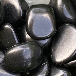 May include: A close-up shot of a pile of polished, black river rocks. The smooth stones have a glossy sheen, reflecting light. The rounded shapes vary in size, creating a natural, organic texture. These decorative stones are suitable for landscaping or crafts.