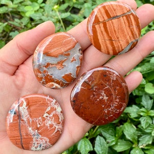 May include: Four red jasper palm stones with white and brown patterns. The stones are smooth and polished.