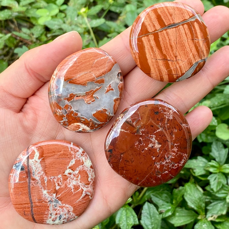 May include: Four red jasper palm stones with white and brown patterns. The stones are smooth and polished.