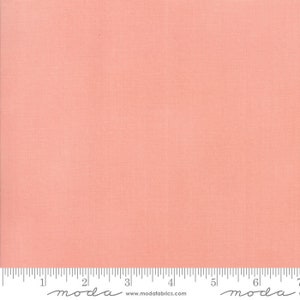 May include: A solid peach-colored fabric with a subtle woven texture. The fabric is evenly lit, showing a consistent color across the surface. A ruler is placed at the bottom, with markings in inches. The fabric is from Moda Fabrics.