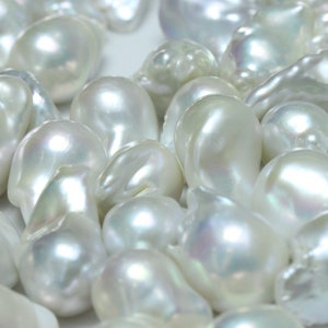 May include: A collection of white baroque pearls with an iridescent sheen. The pearls are various shapes and sizes, and some have a slightly irregular shape.