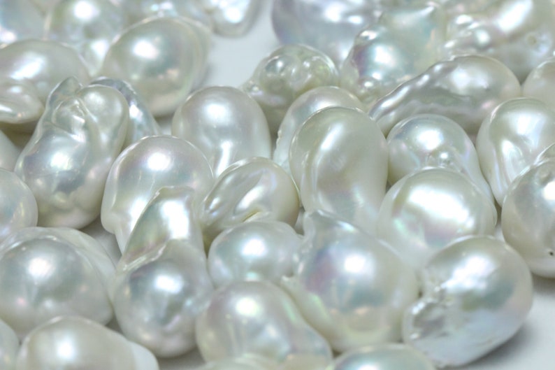 May include: A collection of white baroque pearls with an iridescent sheen. The pearls are various shapes and sizes, and some have a slightly irregular shape.
