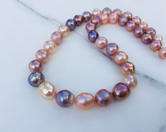 May include: A strand of baroque pearls in shades of pink, purple, and white. The pearls are strung on a clear thread and are arranged in a graduated pattern.