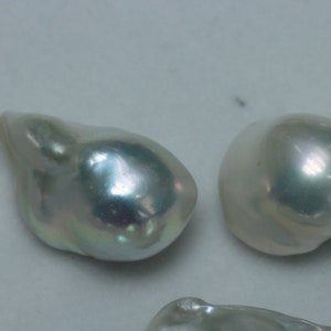 May include: Three iridescent white pearls, two are round and one is an irregular teardrop shape.