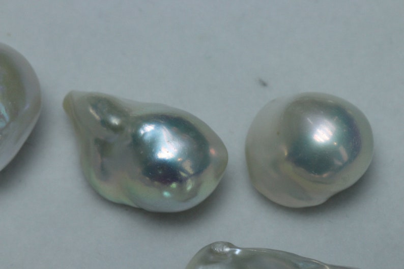 May include: Three iridescent white pearls, two are round and one is an irregular teardrop shape.